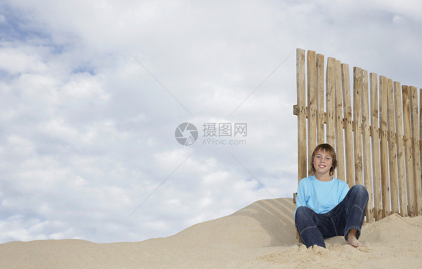 坐在沙沙滩上木栅栏旁边的年轻男孩全长肖像图片