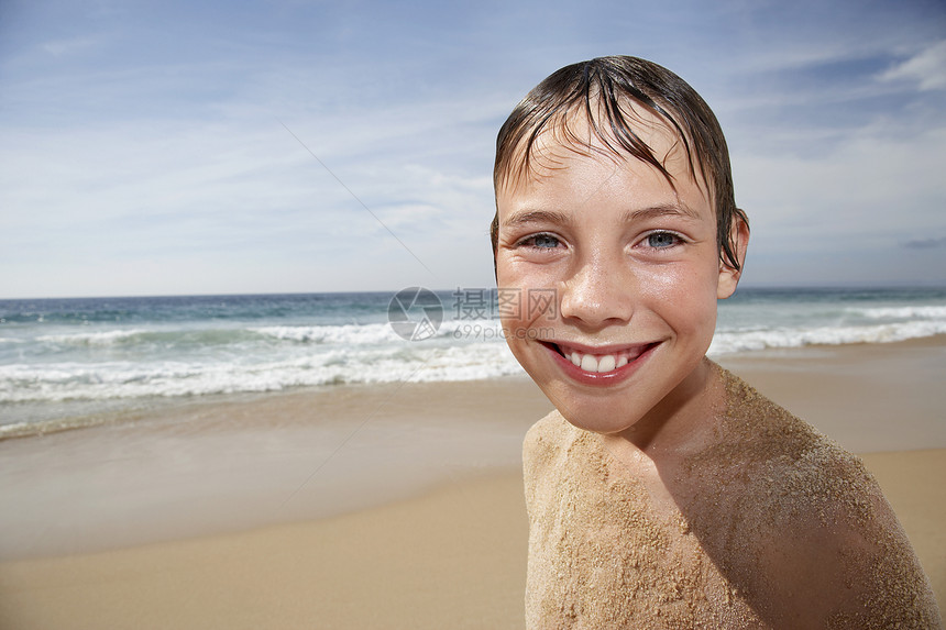 穿着沙沙在海滩上笑脸的无衬衣男孩近身肖像图片