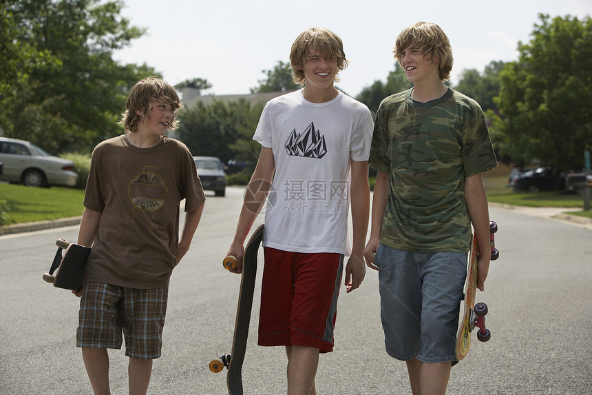 三名十几岁的兄弟(13-17岁)在街上步行 手持滑板图片