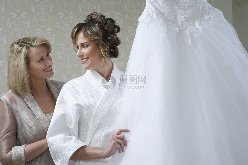 快乐的母亲与新娘 在浴袍触摸婚纱图片