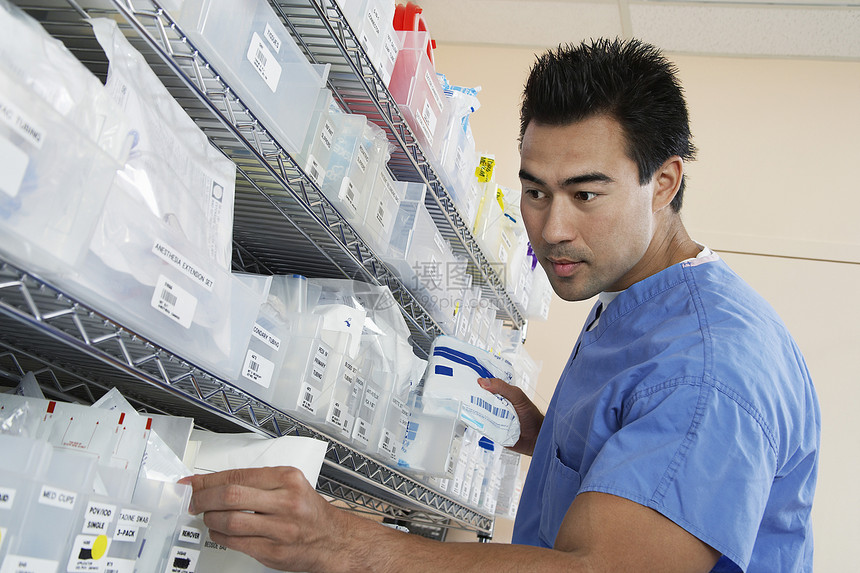年轻男护士在有医疗用品的货架上站立图片