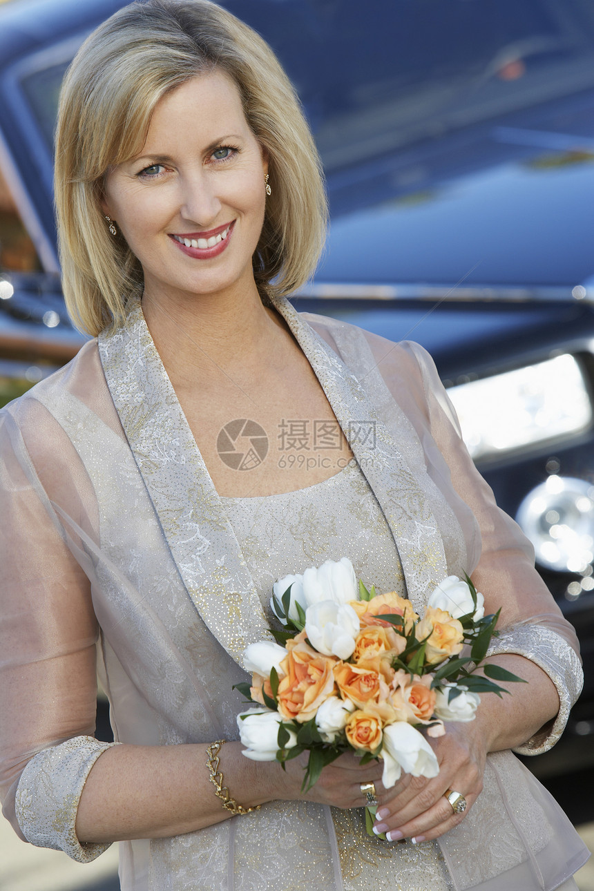一位美女的肖像 在豪华轿车前拿着花束图片