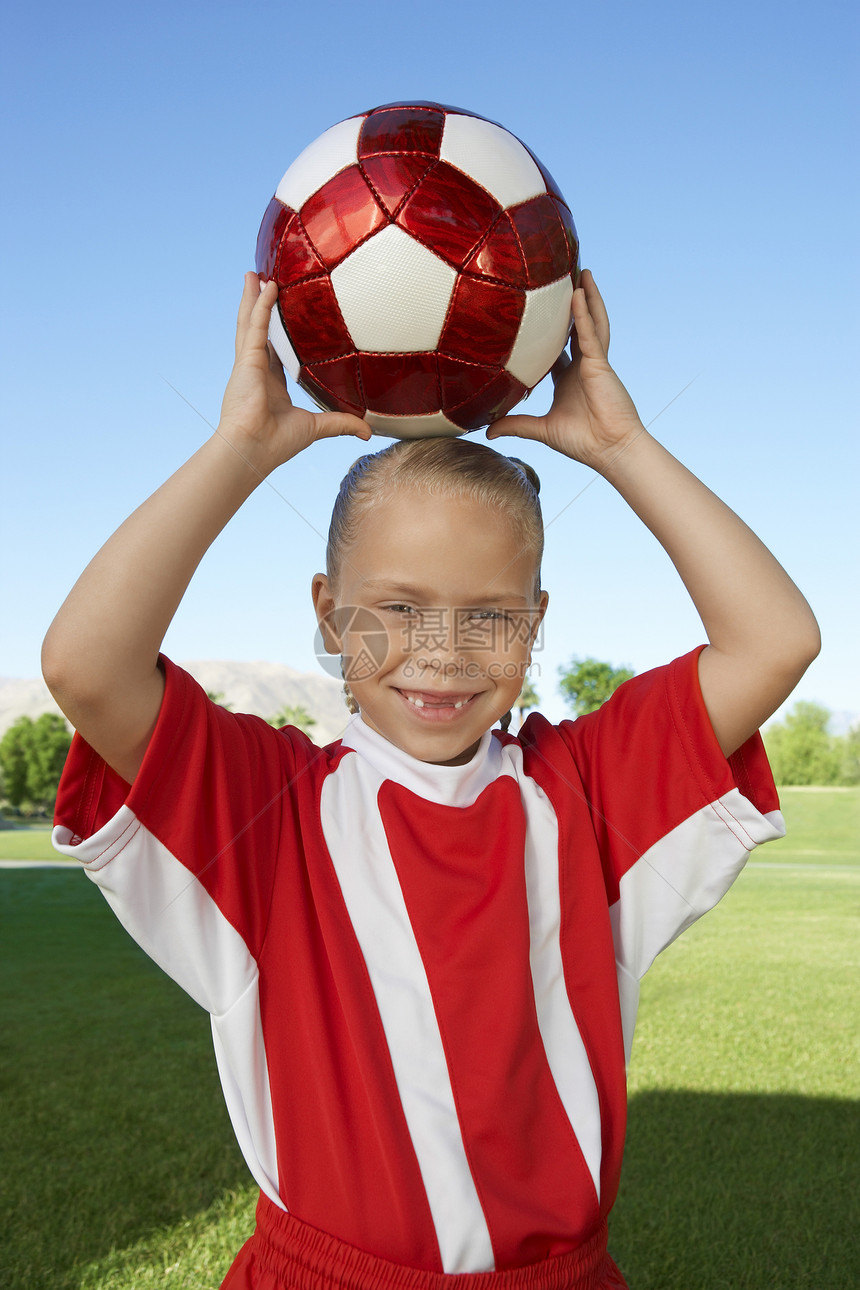 一名年轻女孩的肖像 她高头在田地上举着足球球图片
