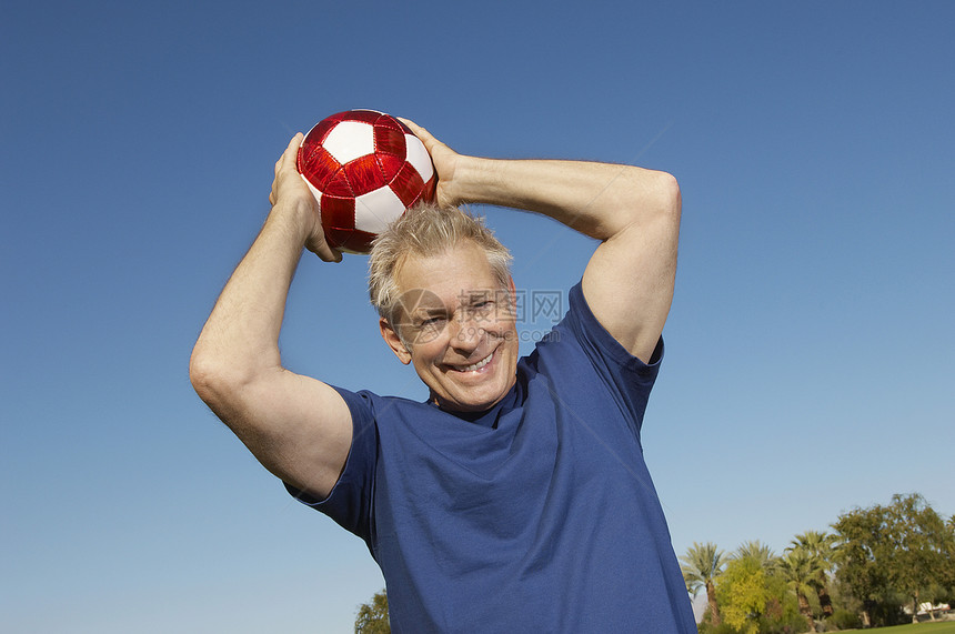一个快乐的老人向蓝天 扔足球球的肖像图片