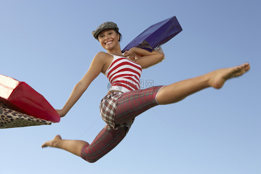一位兴奋的女士用购物袋在蓝天上跳跃的肖像图片