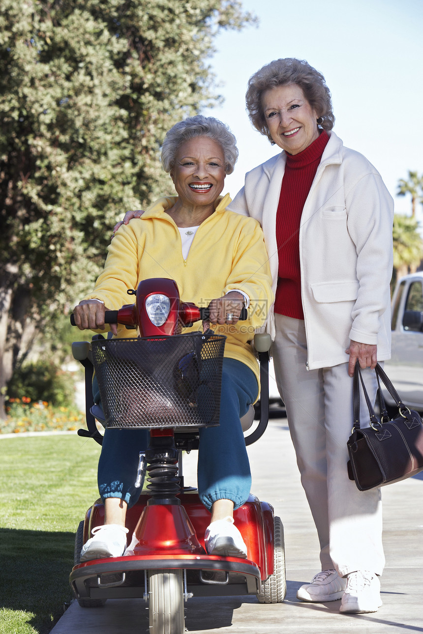 一名残疾高龄妇女坐在摩托摩托车上与朋友站在街上的朋友的肖像图片