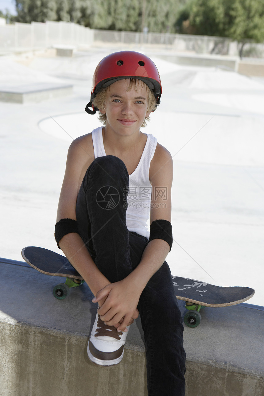 穿着滑板坐在滑冰公园的十几岁男孩的肖像图片