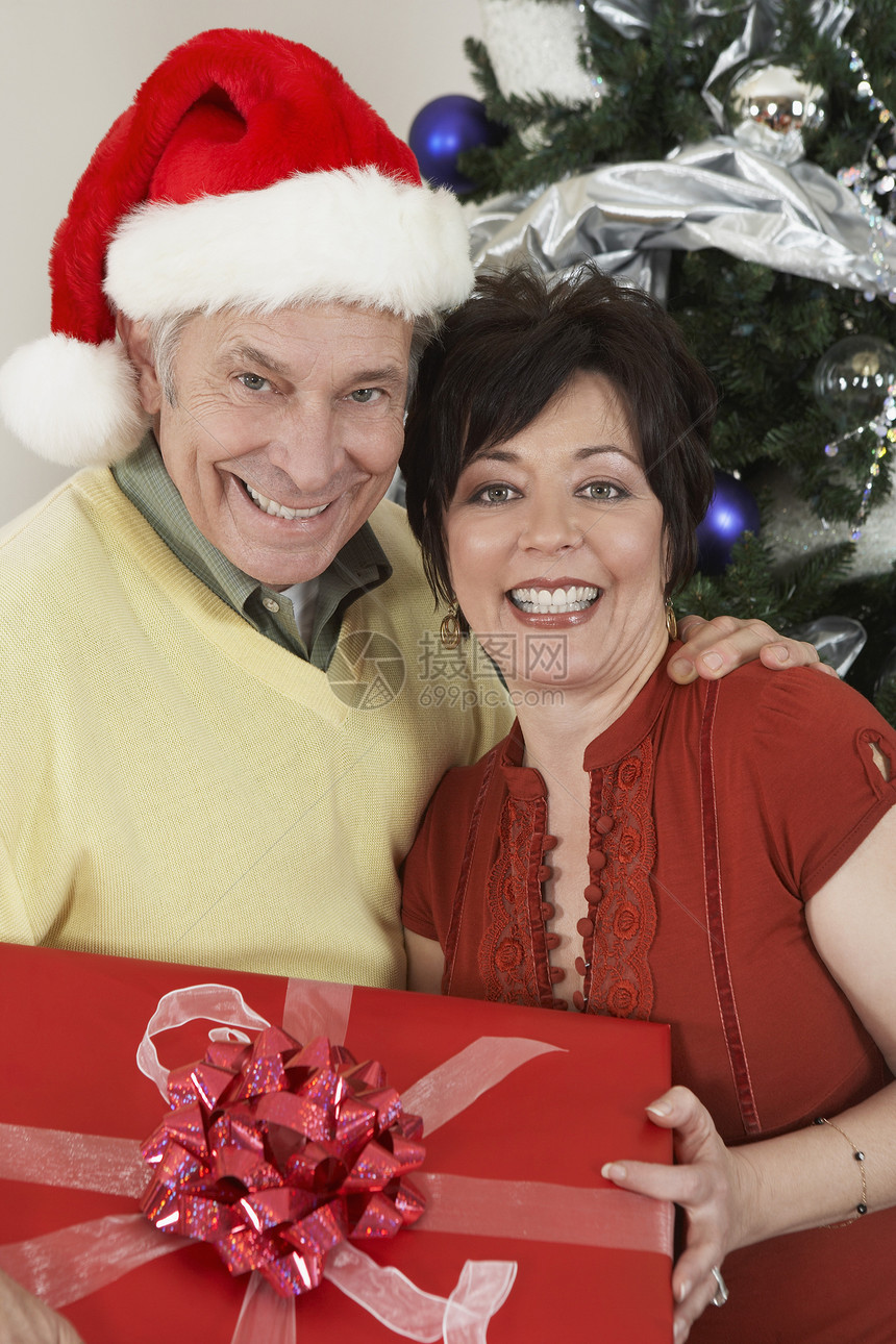 一对幸福的多种族情侣的肖像 拿着礼物盒站在圣诞树前图片