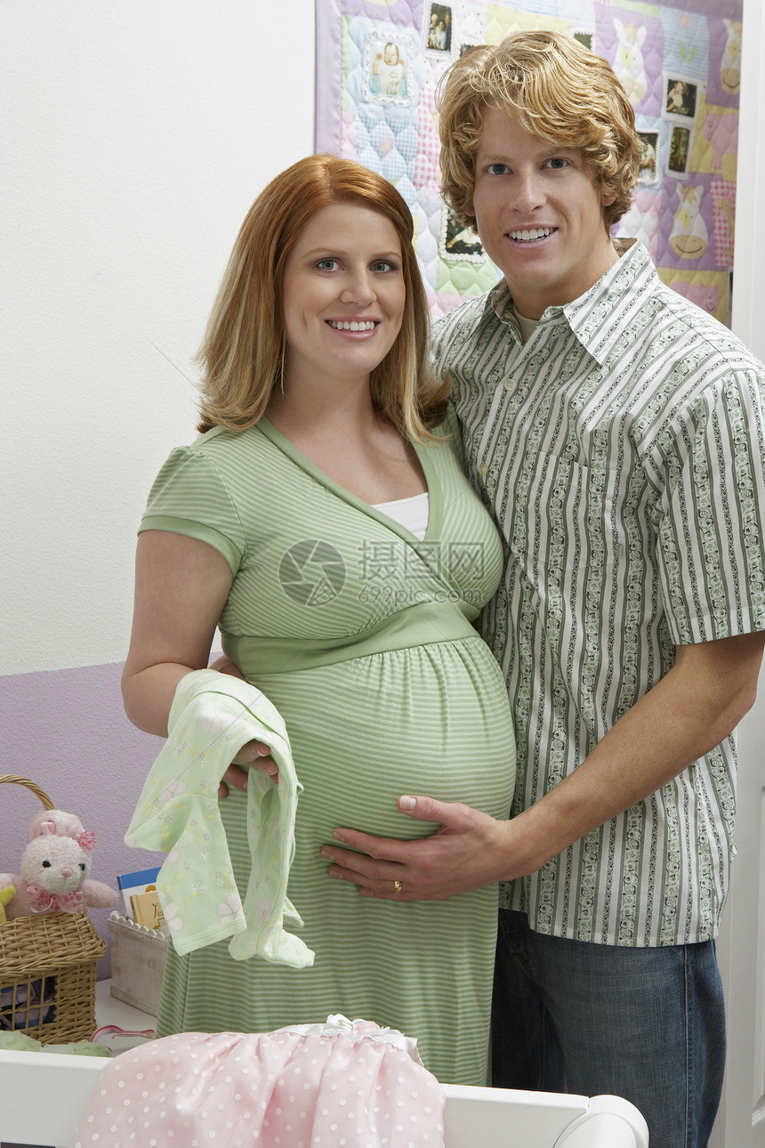 在卧室里穿着婴儿衣的孕妇夫妇的肖像图片