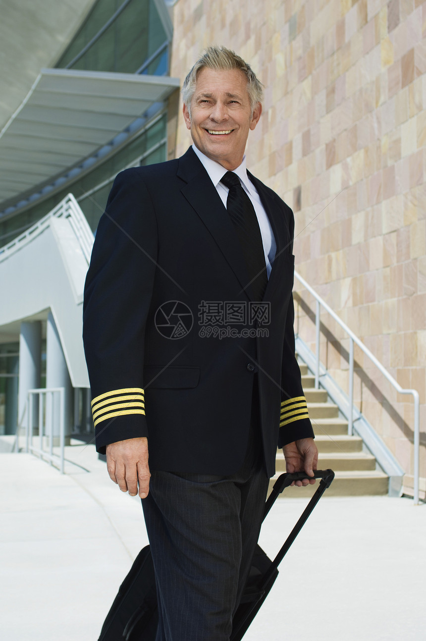 一个微笑的高级航空机驾驶长 在大楼外面拉行李箱的肖像图片
