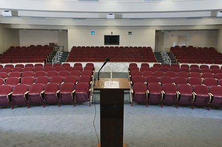 在一个空会议室礼堂按顺序和讲台排列的红椅子背景图片