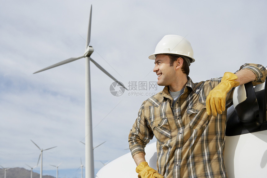 快乐的男工程师站在风力农场的汽车旁站着图片