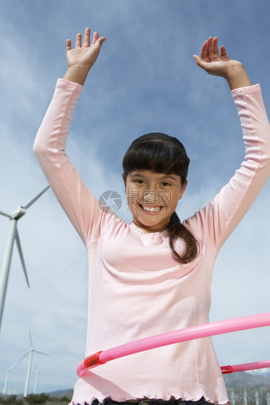 一个快乐的年轻女孩在风力农场玩呼啦圈的低角度景象肖像图片