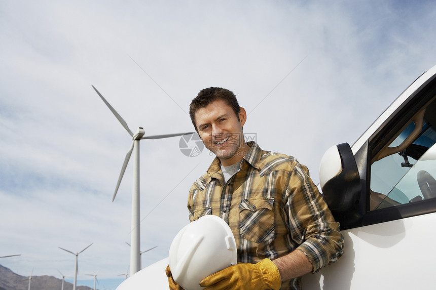 一个快乐工程师的肖像 站在风车农场的汽车旁边图片