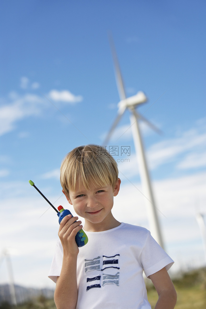 风力农场涡轮机附近一个男孩拿着玩具对讲机的肖像图片