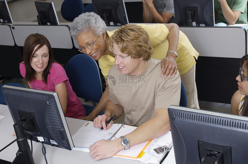 帮助工作在计算机教室的两名学生的老师中年电脑大学小群人微笑合作服装棕榈教学学校图片