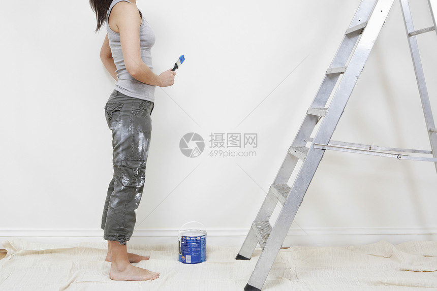在未翻新的房屋中持有油漆刷子的低比例年轻女子图片