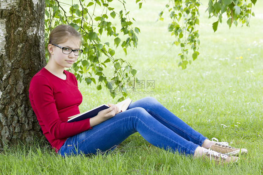 春日在公园读书的年轻女孩腐烂教育眼镜学生阅读空间休息家庭作业草地牛仔裤图片