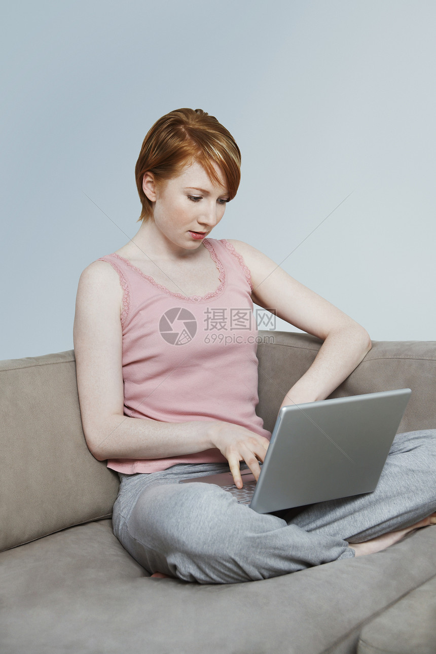 在沙发上使用笔记本电脑的妇女一人女士黄色专注影棚短发技术闲暇工作室头发图片
