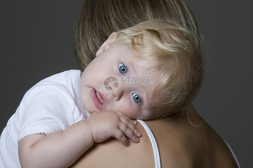 在灰色背景下在母亲的臂膀中休息的女婴紧闭图片