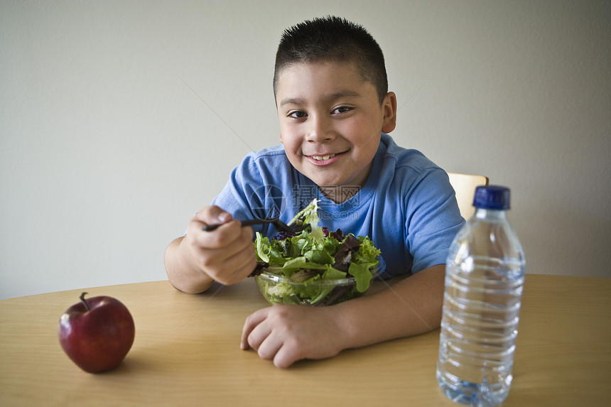 坐在书桌和吃沙拉的十至十(10-12)岁男孩图片