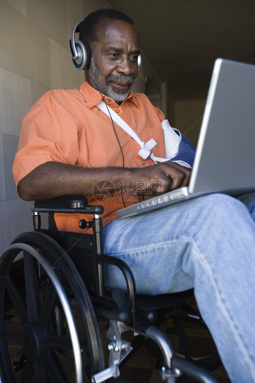 坐在轮椅上听音乐和使用笔记本电脑的老年男子图片