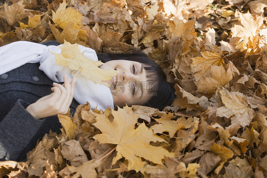 女人躺在公园的树叶上叶子中年休闲服装活动外套黑发围巾微笑保暖图片