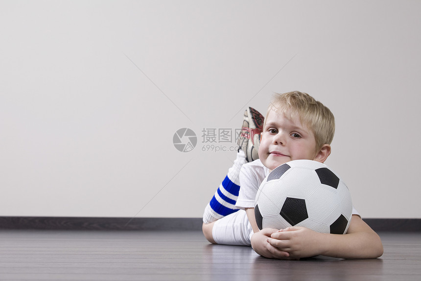 男孩躺在地板上 拿着足球球肖像微笑童年短发快乐爱好头发眼神运动青春期影棚图片
