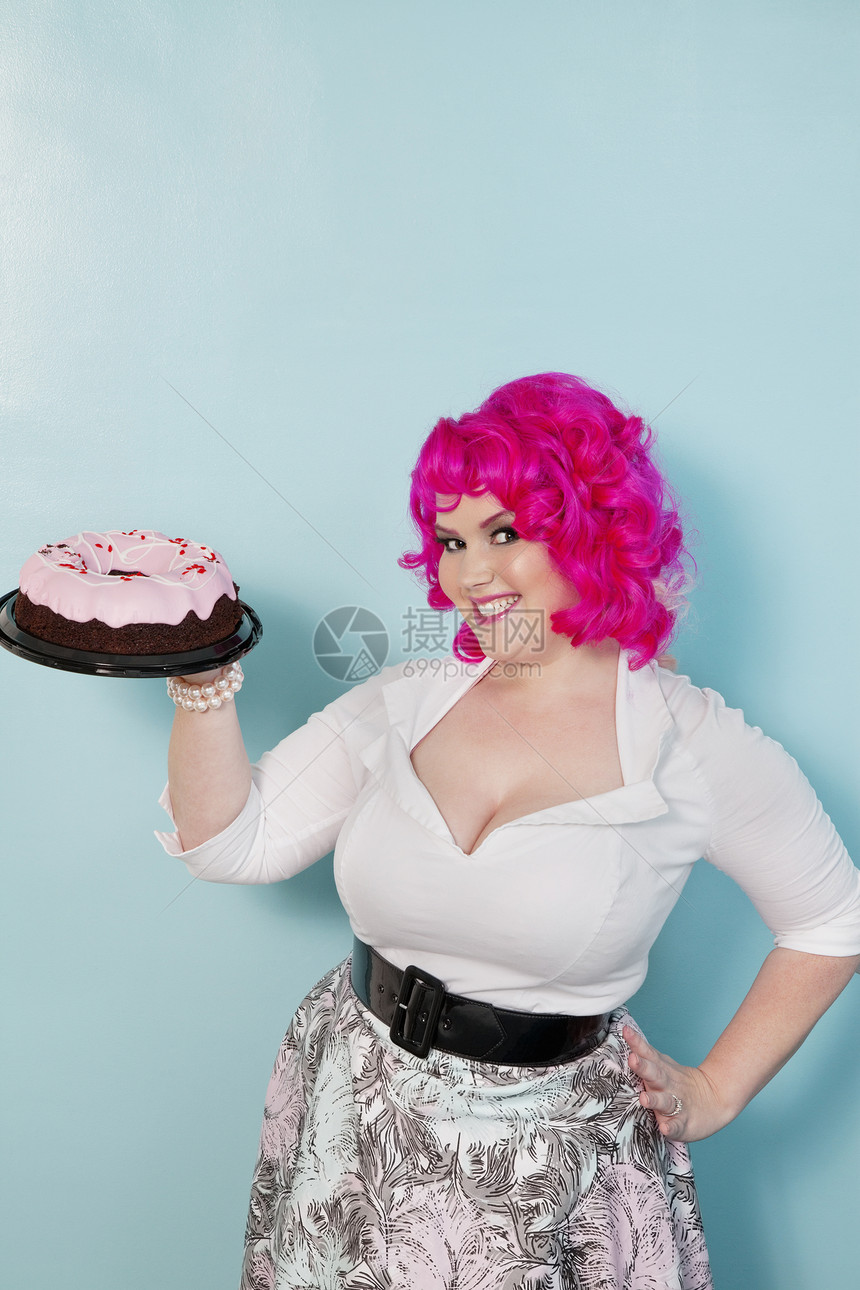 年轻女人的肖像 手站在臀部 拿着蛋糕在彩色背景上图片