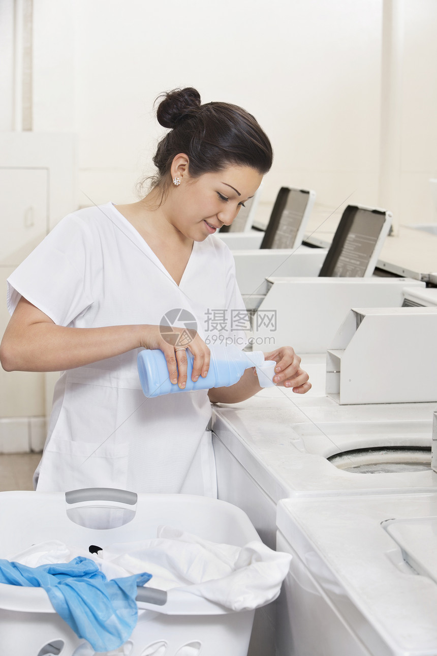 快乐的年轻女雇员在洗衣机洗衣机中倒洗涤剂图片