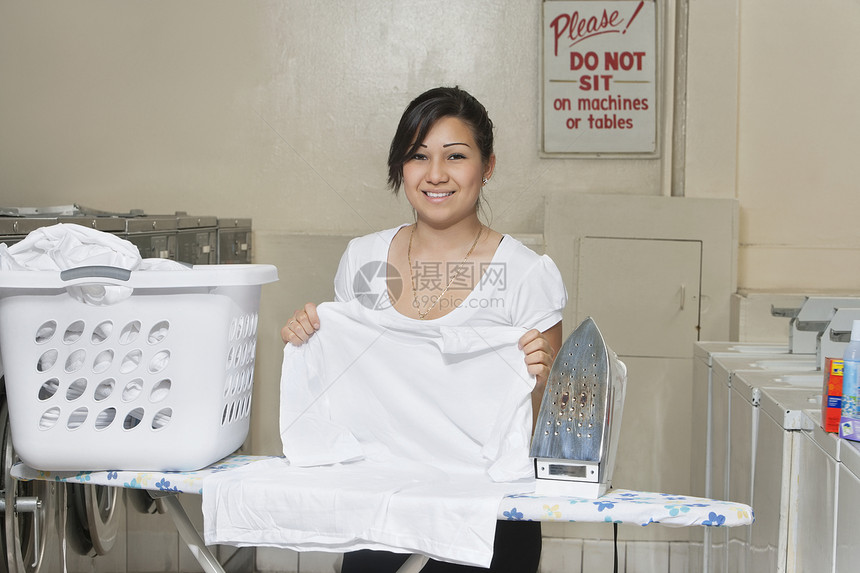 一位快乐的年轻雇员在洗衣店熨衣的肖像图片