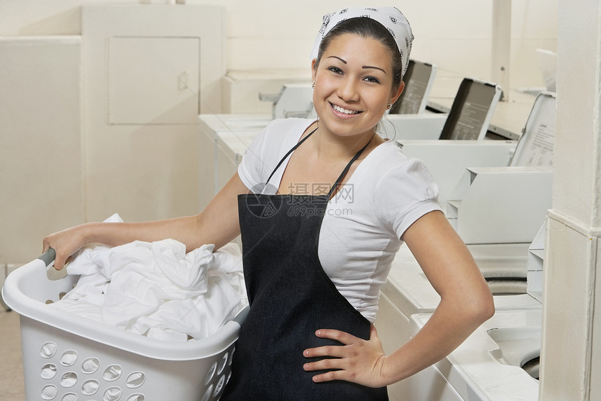 一位快乐的年轻女雇员携带洗衣篮在洗衣店的肖像图片