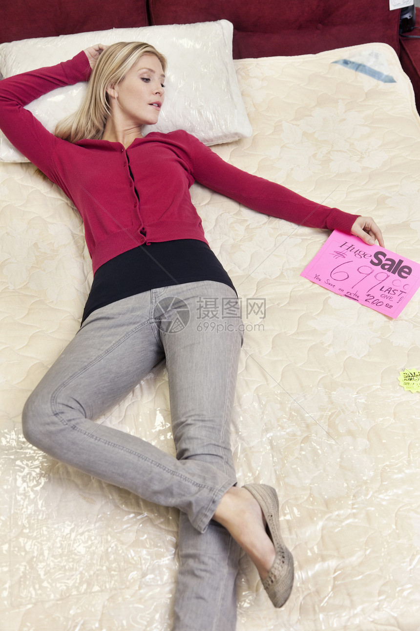 在家具店新床垫上躺着的年轻妇女图片