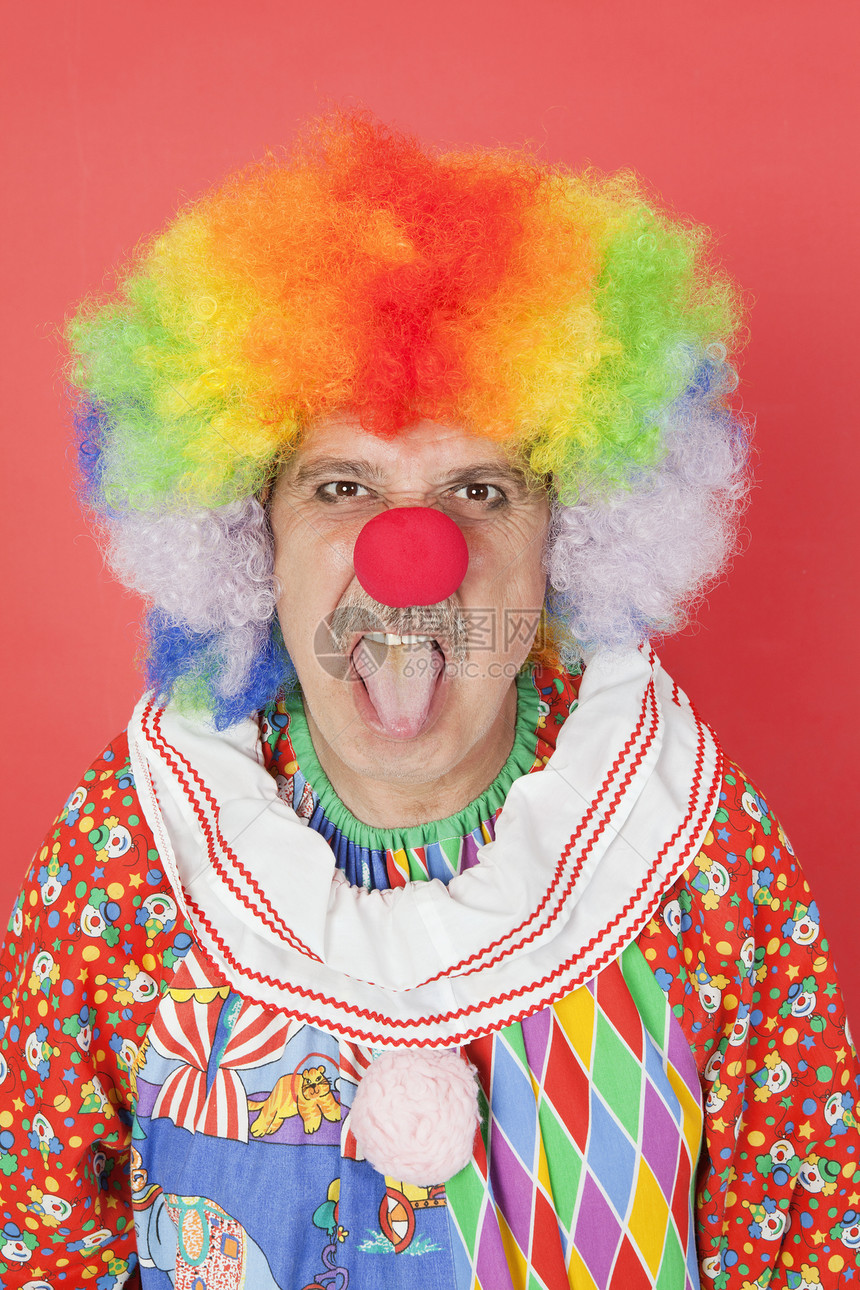 红色背景的男性高龄男小丑用舌头露出舌头的肖像图片