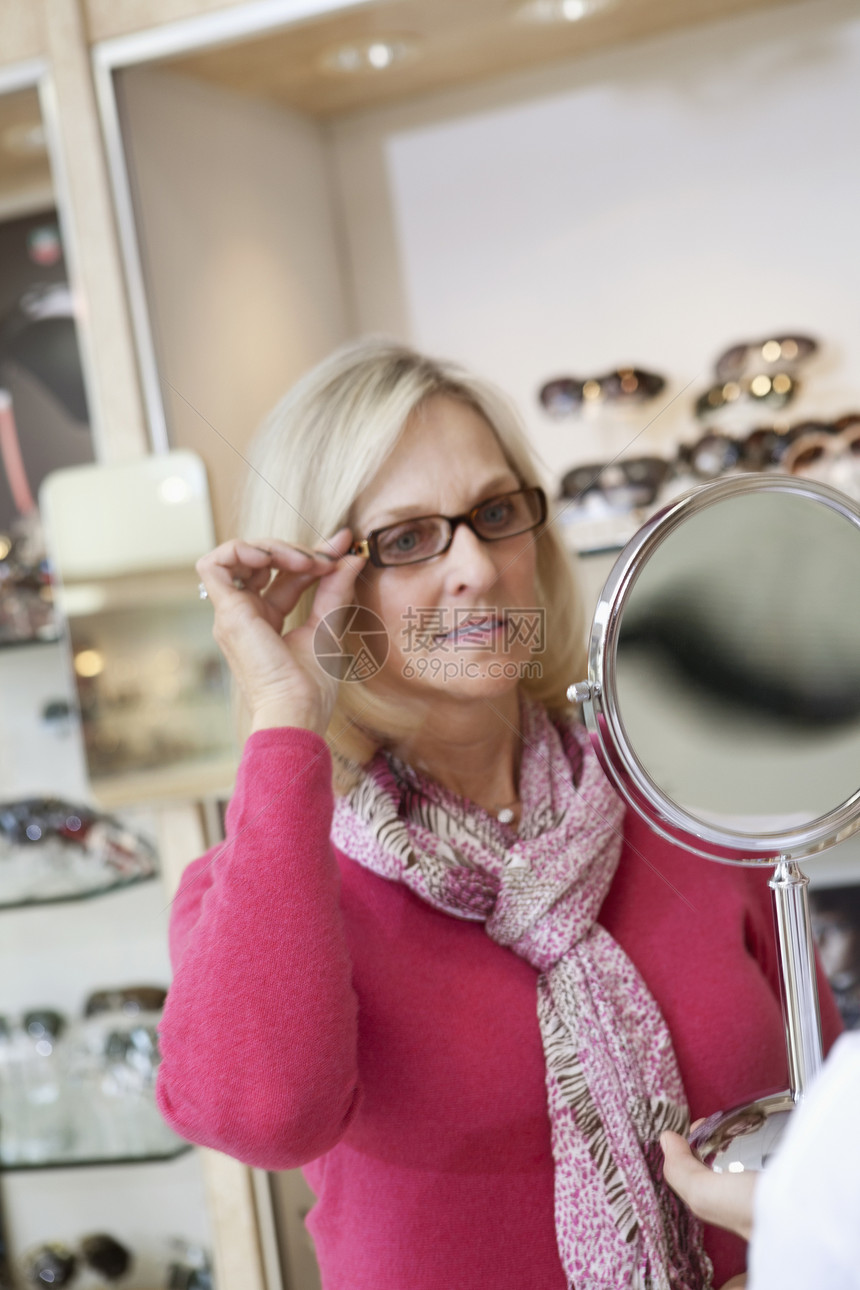 高级女子在商店里看着手镜子时戴眼镜试戴眼镜图片