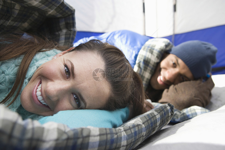 躺在帐篷中睡袋中的一对微笑的年轻夫妇的肖像图片