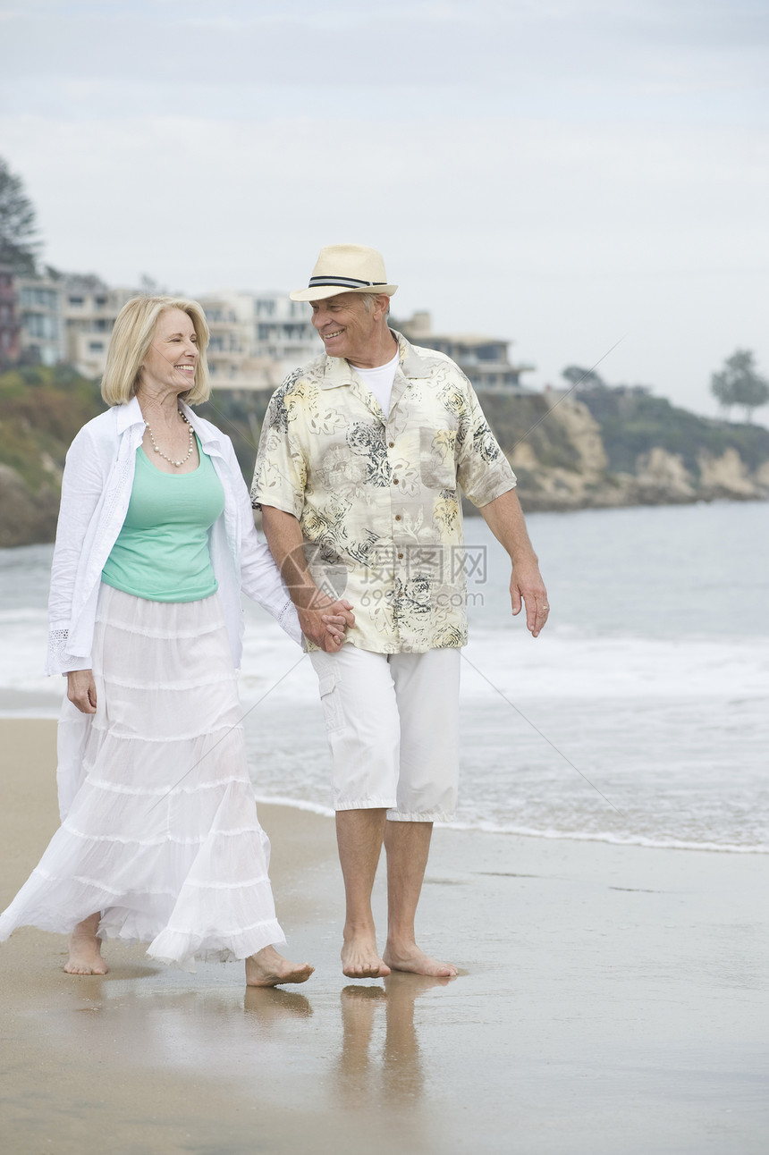 年长夫妇在海滩上手牵手散步两个人团结男人短裤微笑男士退休太阳帽女士成人图片