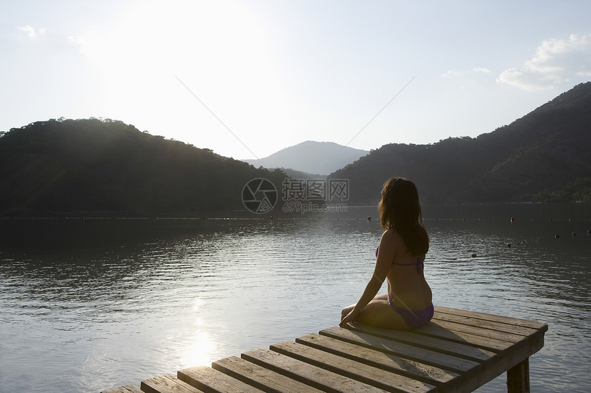 年轻女子在黎明时坐在湖边的码头上图片