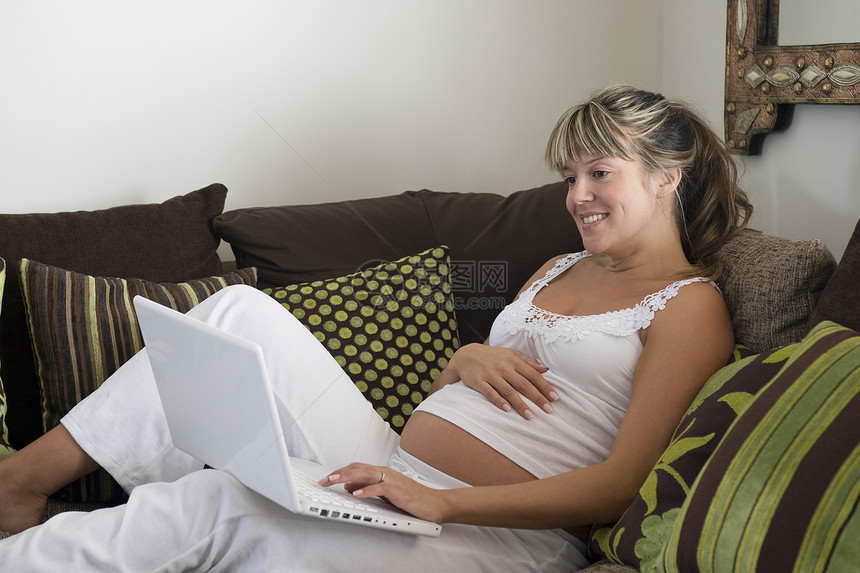 孕妇用笔记本电脑靠在沙发上图片