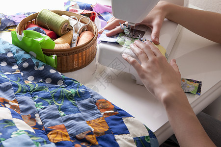 年轻妇女坐在缝纫机上做杂工女子女士桌子成人人类工艺专注纺织品背景图片