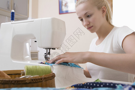 年轻妇女坐在缝纫机上做杂工缝纫女士工艺控制纺织品头发家居创造力背景图片