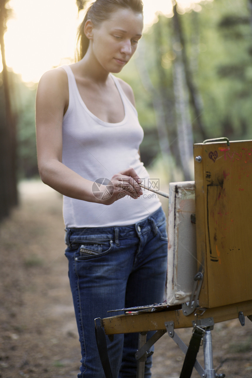 艺术家站在清扫森林的画布上绘画长度牛仔裤双肩女子创造力学生画笔艺术金发女郎外表图片