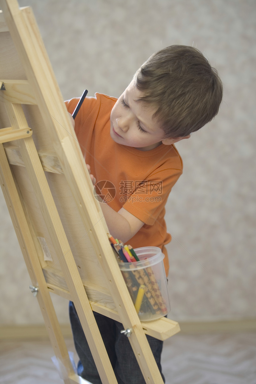 一个小男孩站在画布的边缘 用一罐彩色铅笔在画布上作画创造力男生孩子橙色童年艺术孩子们绘画男孩们蜡笔图片