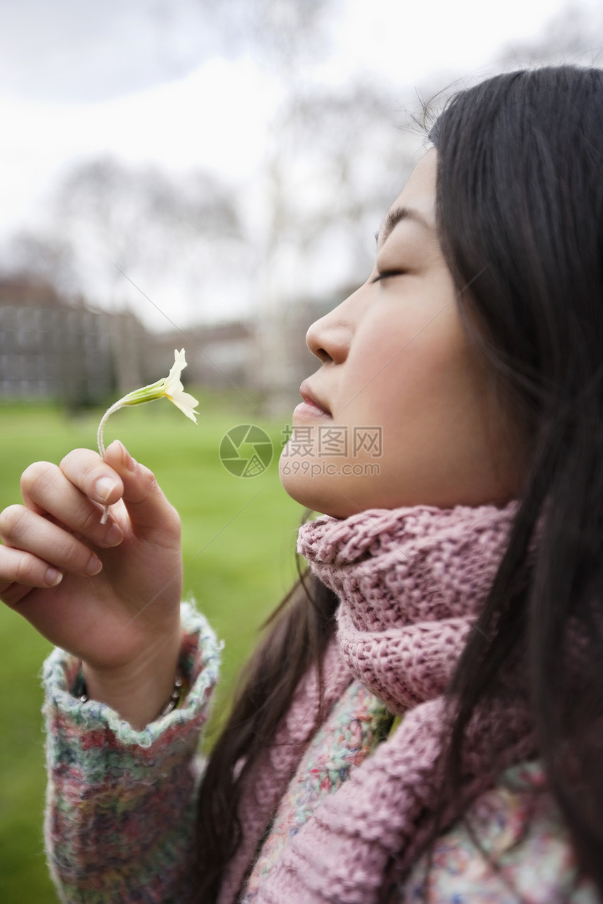 一位亚洲年轻女子在公园闻花香的侧面景象图片