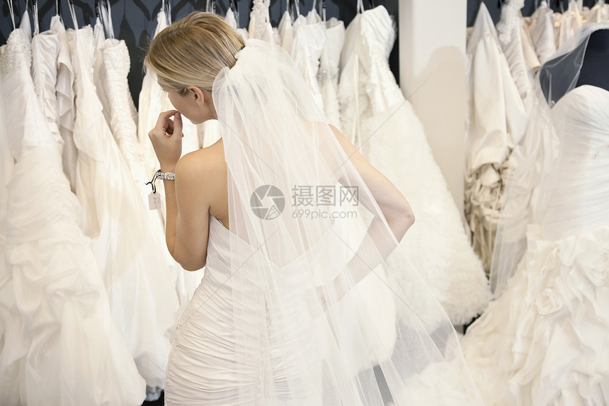 一个穿着婚纱的年轻女子的背影 看着在商店展露的新娘礼服图片