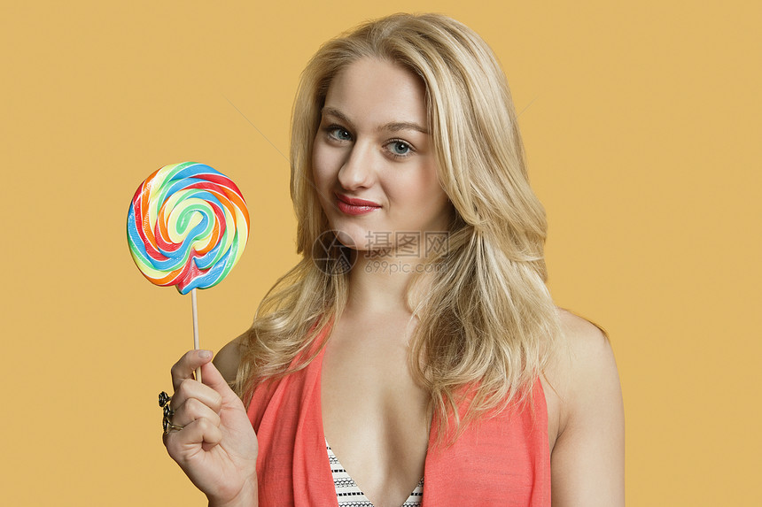 一位年轻金发女子的肖像 拿着棒棒棒棒糖在彩色背景之上图片