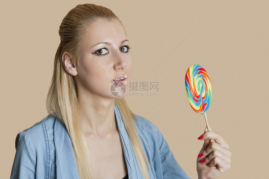 一个金发女人的肖像 嘴唇喷满了口水 把棒棒棒糖压在彩色背景上图片