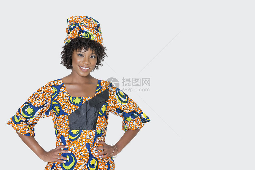 身着非洲印刷服装的年轻女性肖像 在灰色背景上手举臀站立图片