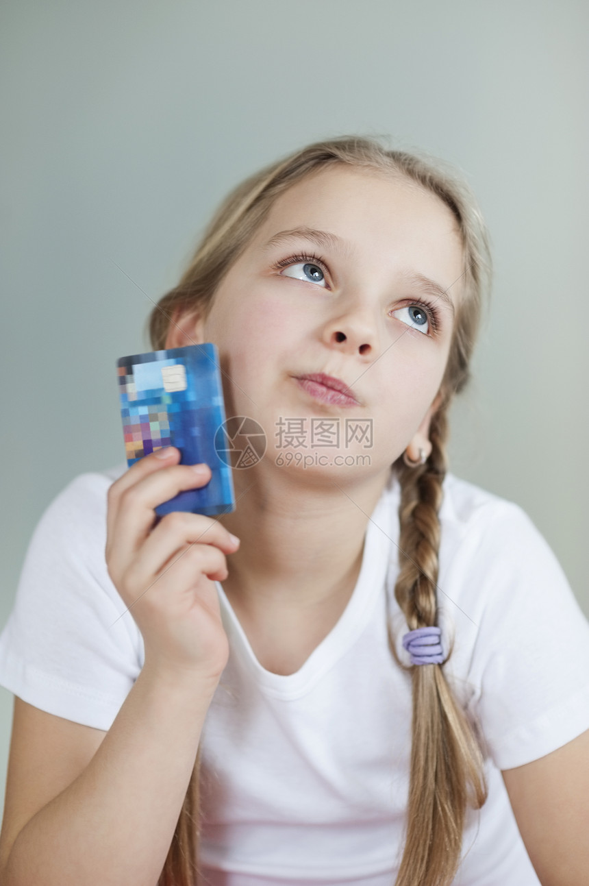 带着灰色背景信用卡的有想象力的年轻女孩图片