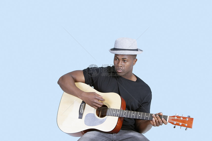 非洲裔美国青年男子在浅蓝背景下弹吉他游戏浅蓝色衣服成人休闲服装成年乐器吉他手音乐帽子图片
